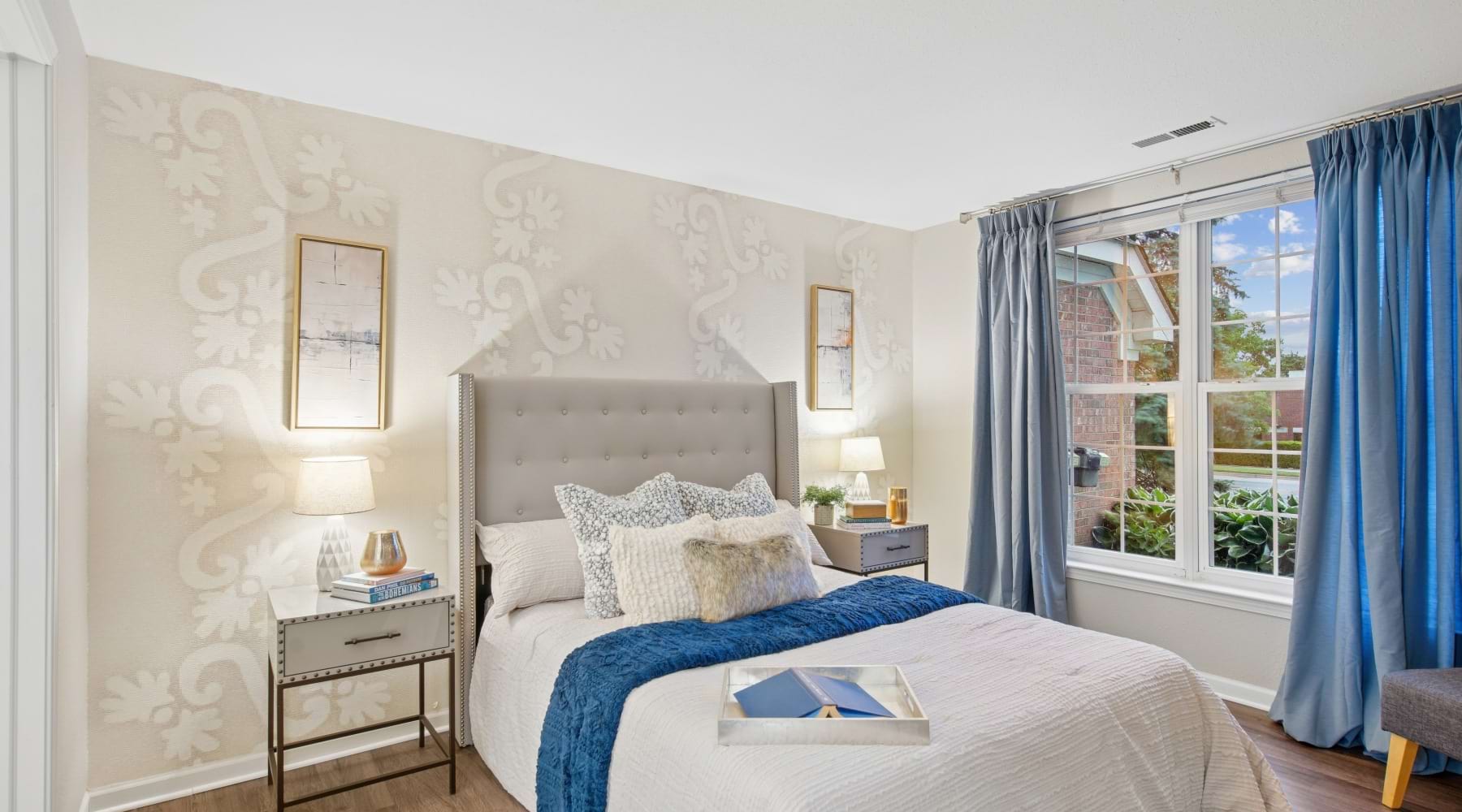 A bedroom with a bed and two side tables, with views of a bathroom at The Chapman apartments in Rochester, MI.
