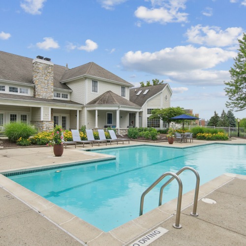 A pool with lounge chairs and greenery in the background at The Chapman Rochester apartments Michigan.