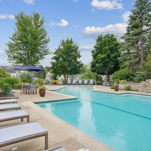 A pool with lounge chairs and greenery in the background at The Chapman Rochester apartments Michigan.